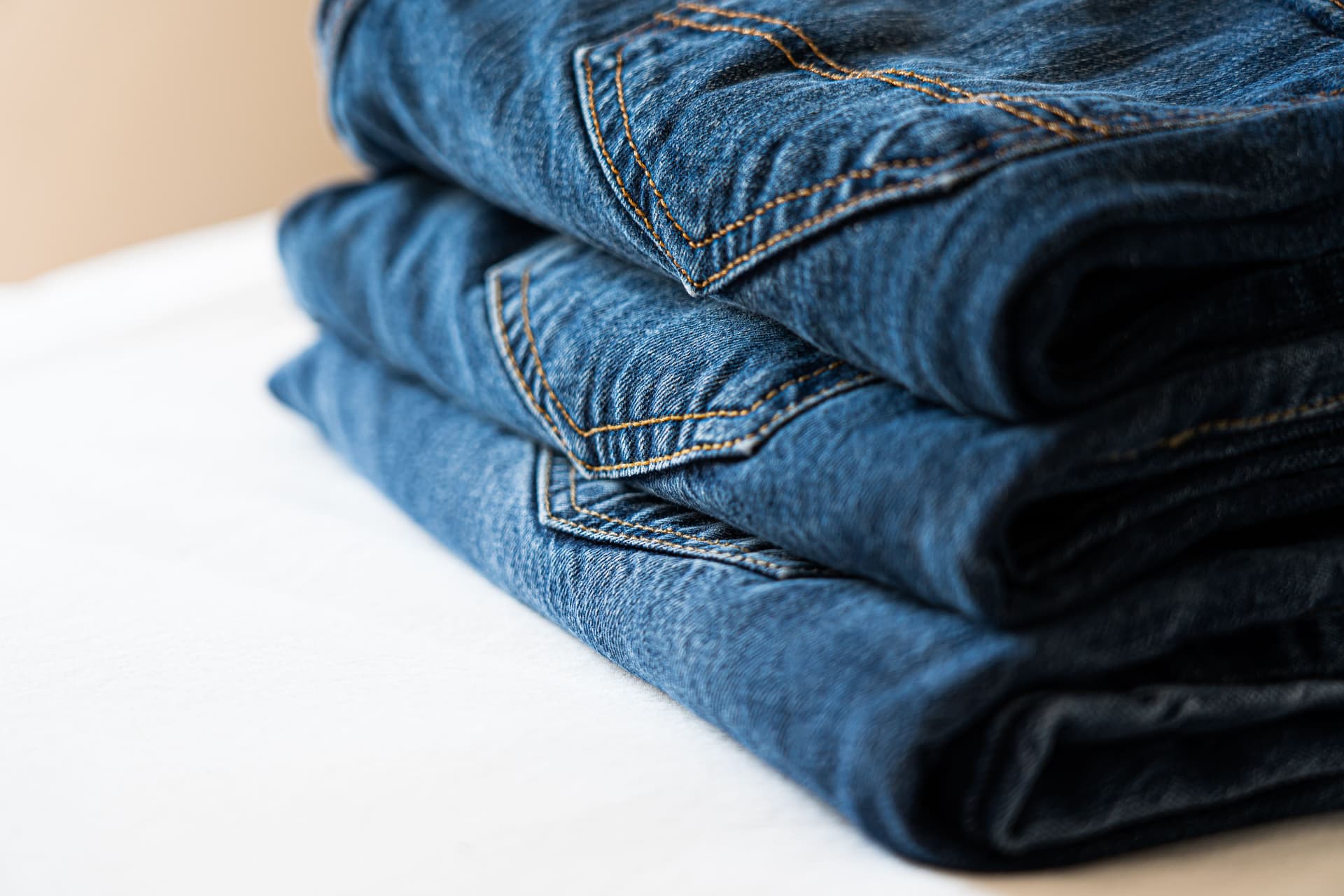 A stack of neatly folded blue denim jeans photographed close enough to show the stitching.